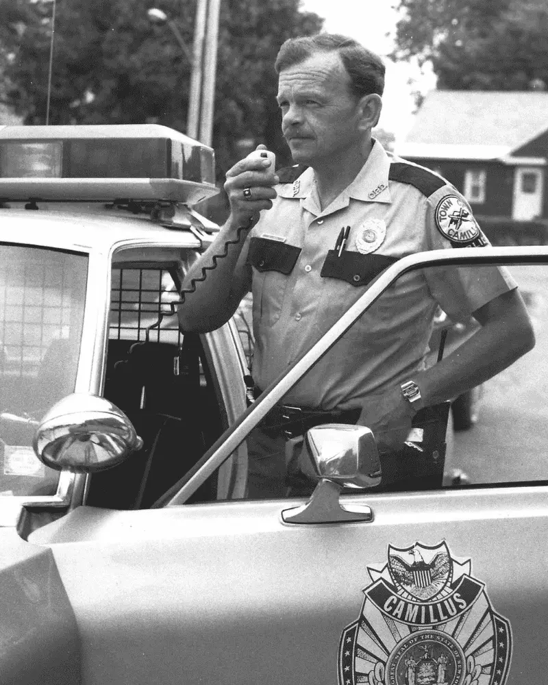 Old image of Camillus Police Officer standing by his cruise talking on his radio